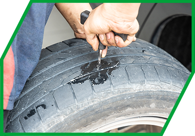 Mechanikerhände ziehen Flicken per T-Griff in die Reifen-Lauffläche